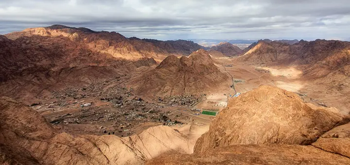 A sweeping view from Mount Sefsafa, showing the mountain-ringed town of Saint Catherine below, with golden light casting shadows over the rugged terrain — a stunning moment on a classic St Catherine Hike.