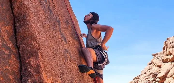 Top 10 things to do in Sinai in 2025 A climber ascends a rugged granite wall in the mountains of Saint Catherine, using ropes and gear, with sunlit peaks and desert terrain stretching out in the background.