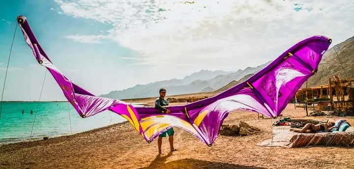 Top 10 things to do in Sinai in 2025 A man stands on the sandy shore of Dahab, adjusting his kite or windsurfing gear under clear skies, with turquoise water and steady coastal winds creating the perfect setting for wind sports.
