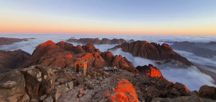 View from Mount Sinai after sunrise, with golden light illuminating clouds below the mountain peaks