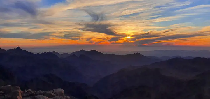Sunset over Mount Abbas Basha in the Sinai Mountains, casting golden light on rugged peaks and deep valleys.