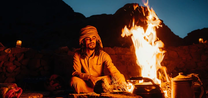 A Bedouin from the Sinai Hikes team sitting beside a fire preparing tea in the Egypt Mountains.