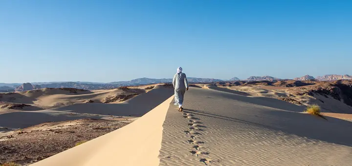 Barefoot Bedouin man walking across the sandy terrain of the Sinai Desert, to Egypt Mountains side.