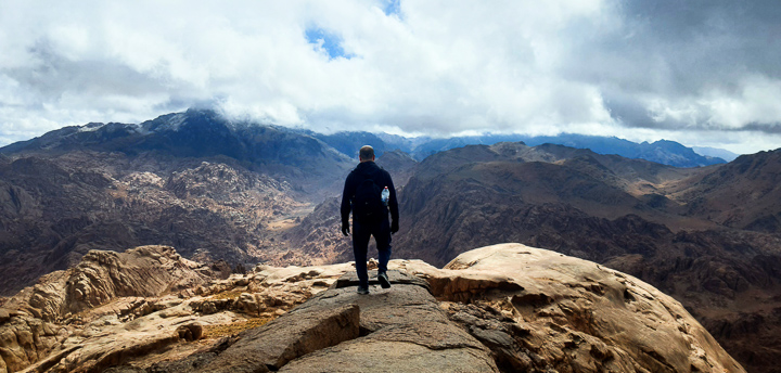 Hiker descending rocky trail from Mount Abbas Basha in South Sinai toward Abo Mahashor.