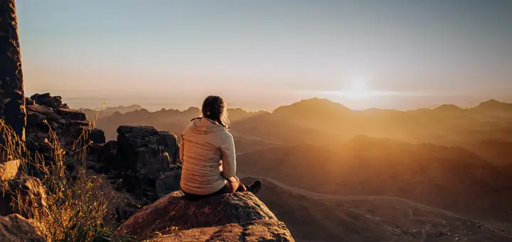 Hiker standing on a rocky ridge in the Sinai Mountains at sunrise, overlooking the vast desert landscape of Egypt.