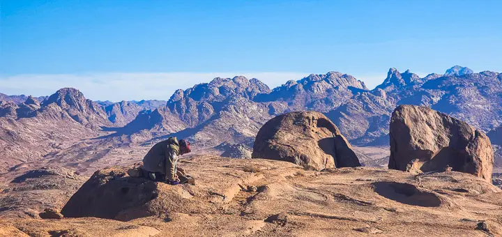 Bedouin guide gathering firewood on the slopes of Mount El Banat in the Egypt Mountains, surrounded by dry rocky terrain.