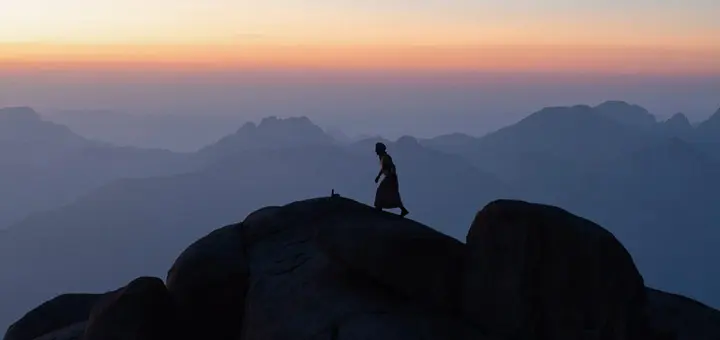 Bedouin guide standing on rocky ground in Mount Shayb El-Banat in the Egypt Mountains, surrounded by high desert cliffs and silence.