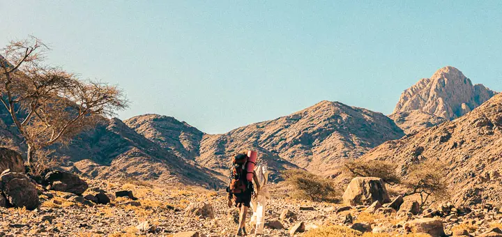 Hiker and Bedouin guide trekking toward Mount Serbal through the rugged terrain of Wadi Feiran, South Sinai.