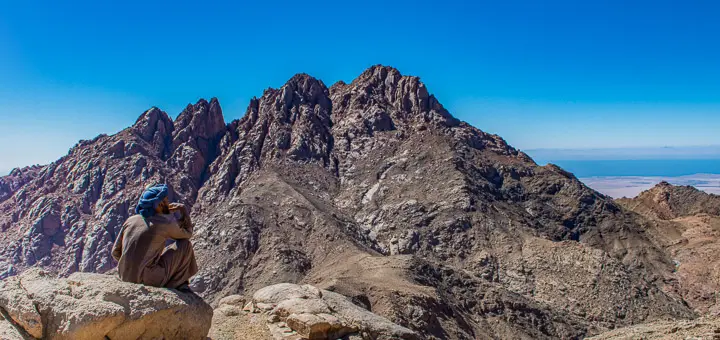 Bedouin guide standing on rocky terrain, gazing toward the distant peak of Mount umm Shomar in the Egypt Mountains.