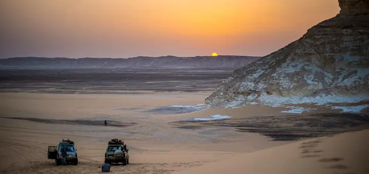 Sunset over Bahariya Oasis with golden light illuminating palm trees, desert cliffs, and sand dunes in Egypt’s Western Desert.